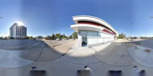 Panoramic view of a modern dental clinic with a curved white facade and red band, glass storefronts, and a parking lot under a clear blue sky.