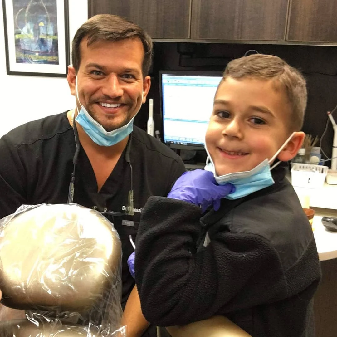 A young patient smiling alongside a member of the clinical team in the treatment room at Loukas Dentistry of Park Ridge, Illinois